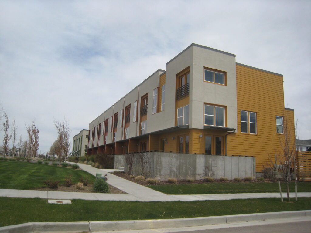 Modern multi-unit residential buildings with varied exterior colors and landscaping, set against a cloudy sky, showcasing urban living.